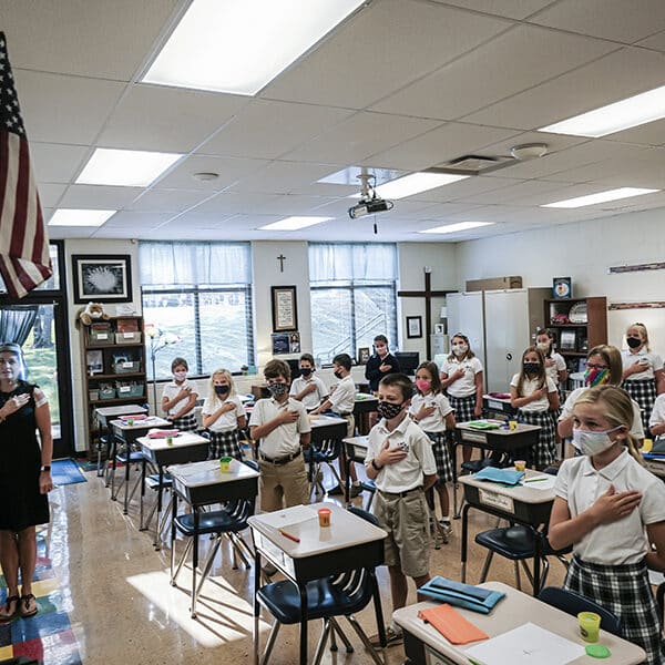 Fourth-grade teacher Kristina Tons, wearing a clear plastic face shield, leads her class in the Pledge of Allegiance.