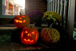 Carved jack-o-lanterns glow at night on the porch steps of a house