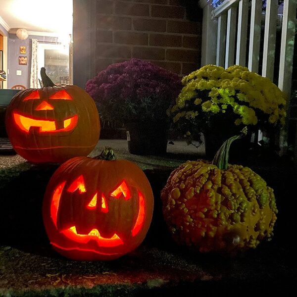 Carved jack-o-lanterns glow at night on the porch steps of a house