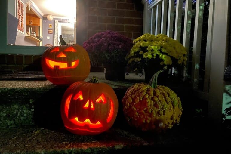 Carved jack-o-lanterns glow at night on the porch steps of a house