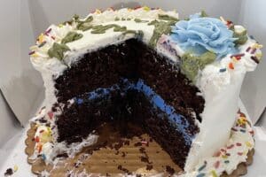 A chocolate cake with white frosting is sliced so you can see the blue frosting inside