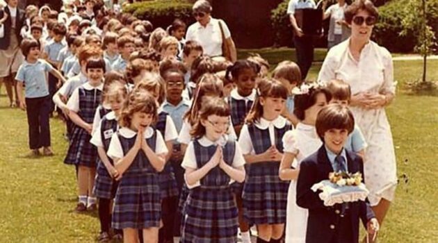 Children in school uniforms walk together with hands folded in a May Procession to honor the Blessed Mother