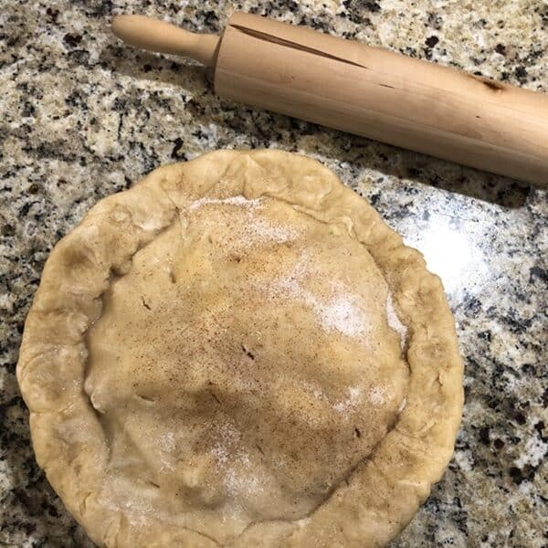 A homemade pie that is ready to bake sits on a kitchen counter next to a rolling pie