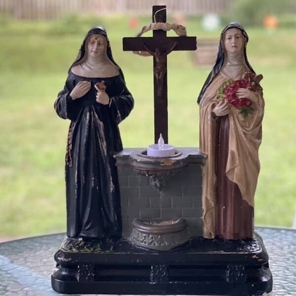 Sculpture of St. Rita and St. Therese with a cross and holy water font at the center sits on a table