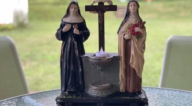 Sculpture of St. Rita and St. Therese with a cross and holy water font at the center sits on a table