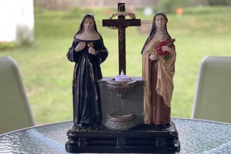 Sculpture of St. Rita and St. Therese with a cross and holy water font at the center sits on a table