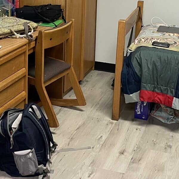 A college dorm room with a backpack, desk, part of a bed