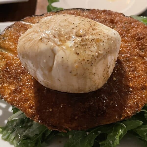 Caprese salad on a plate with a ball of mozzarella on a piece of fried eggplant atop greens