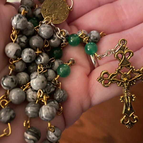 A hand holds a Rosary with a crucifix prominently displayed