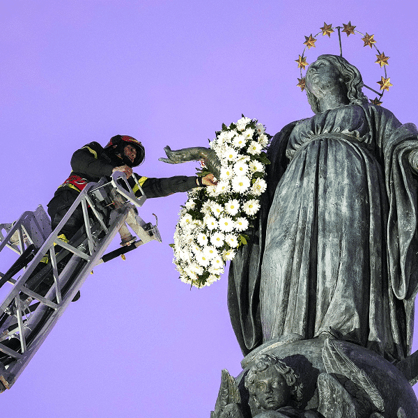 Roberto Leo, a senior firefighter, places a wreath of flowers on a Marian statue
