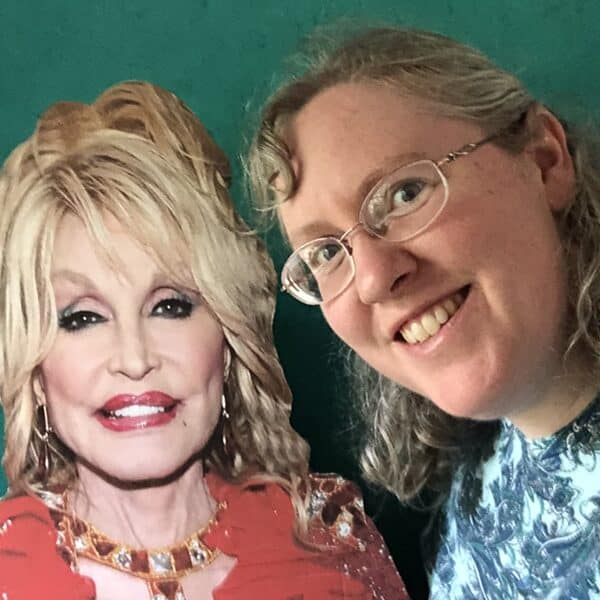 The writer poses with a cardboard cutout of Dolly Parton against a green background