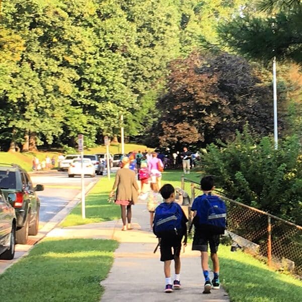 Two boys with backpacks walk on a sidewalk to school