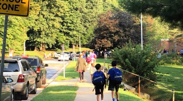 Two boys with backpacks walk on a sidewalk to school