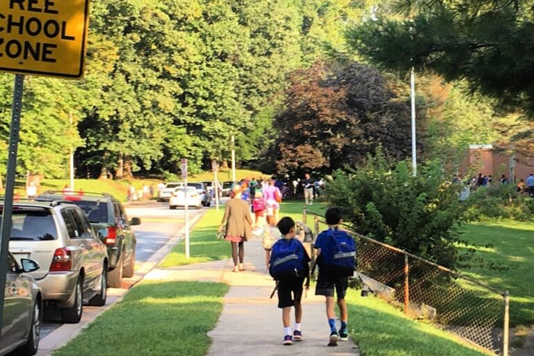Two boys with backpacks walk on a sidewalk to school