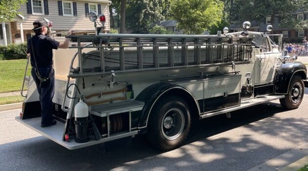Firefighter rides on the back of a vintage fire engine