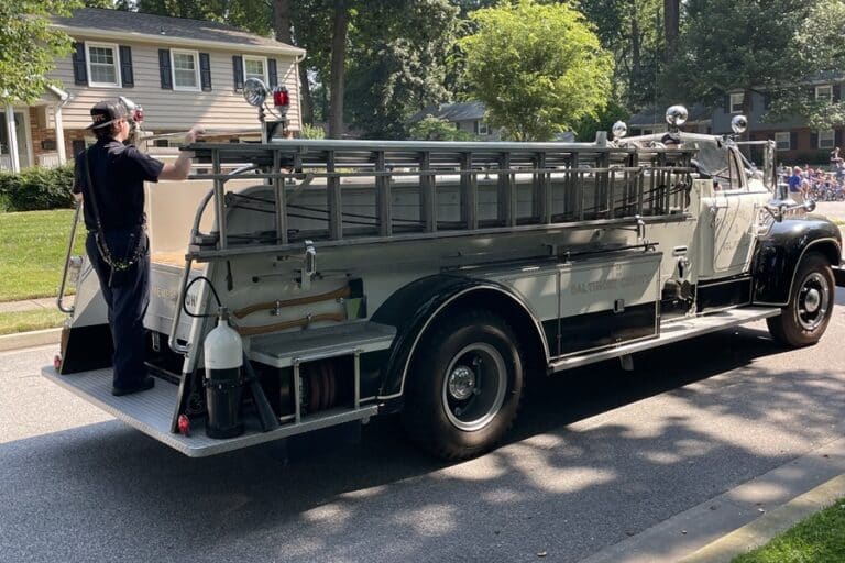 Firefighter rides on the back of a vintage fire engine